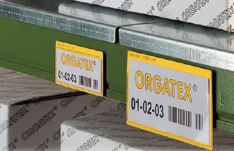 Close-up of an industrial shelf with yellow Orgatex labels. Labels feature barcodes and numbers "01-02-03" on a green metal beam, conveying organization. Lean Factory America Orgatex Visual Management.